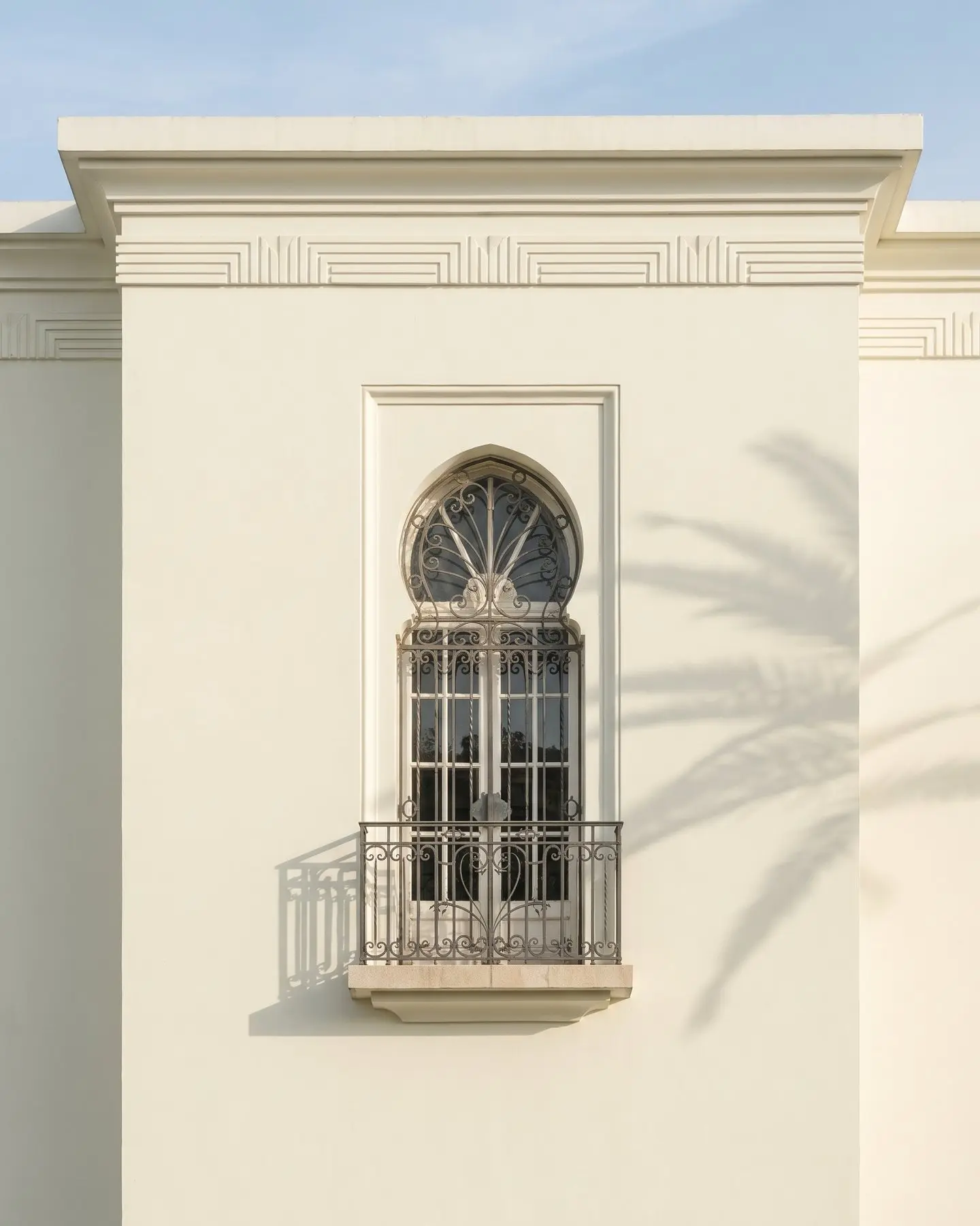 A white Art Deco façade in Casablanca, an arched window with its wrought-iron balcony, the shadow of a palm