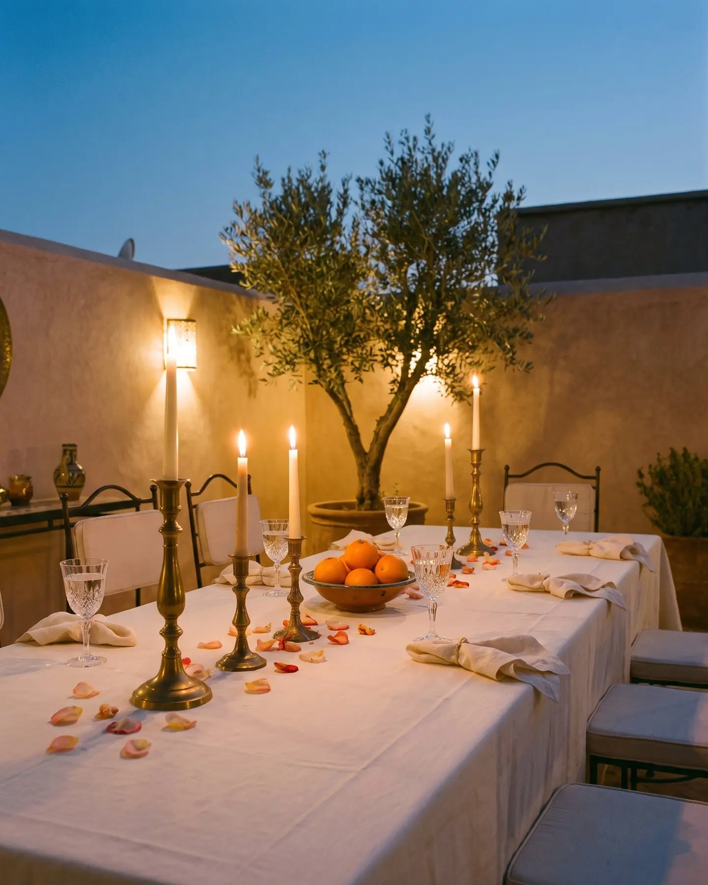 A long table on a riad terrace after dinner, candles in brass candlesticks